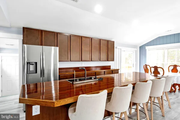 a kitchen with stainless steel appliances kitchen island granite countertop a refrigerator a stove a dining table and chairs with wooden floor