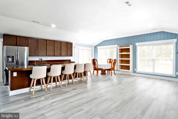 a living room with stainless steel appliances dining table wooden floor and a large window