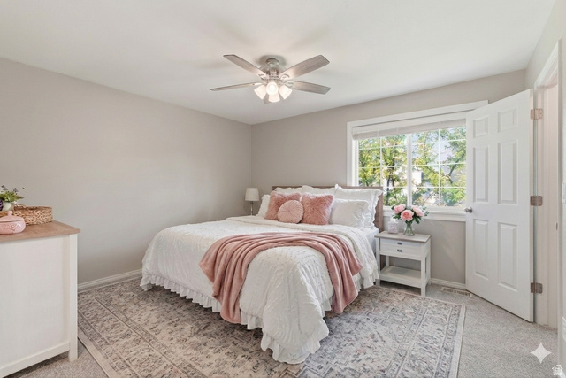 99 Penhurst Place Logan, UT 84341 - Photo 15 of 34 Bedroom featuring light gray wall paint, a ceiling fan with integrated lighting, a large window with white trim, and light-colored carpeting