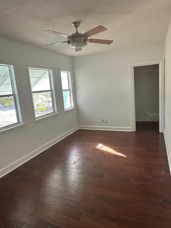 an empty room with wooden floor fan and windows