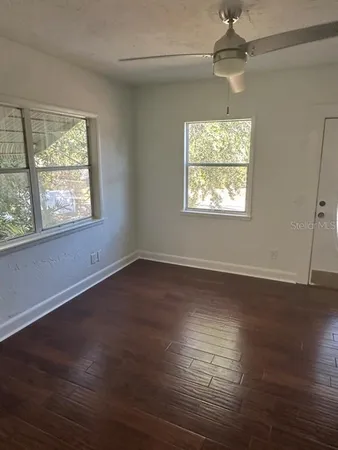 an empty room with wooden floor chandelier fan and windows