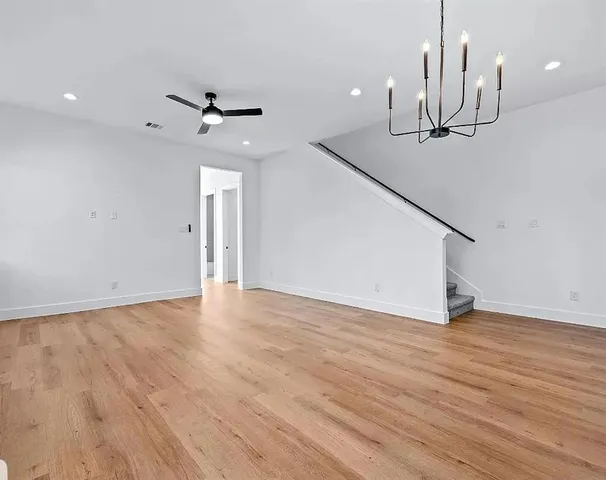 a view of an empty room with wooden floor and a ceiling fan