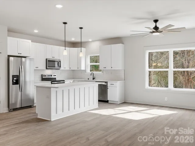 a kitchen with stainless steel appliances kitchen island granite countertop a refrigerator a sink dishwasher a stove and white cabinets with wooden floor