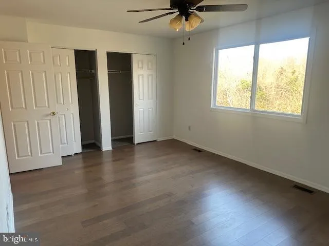 an empty room with wooden floor fan and windows