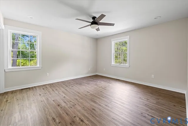 an empty room with wooden floor windows and ceiling fan
