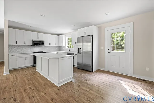 a kitchen with stainless steel appliances granite countertop a refrigerator a stove a sink and white cabinets with wooden floor