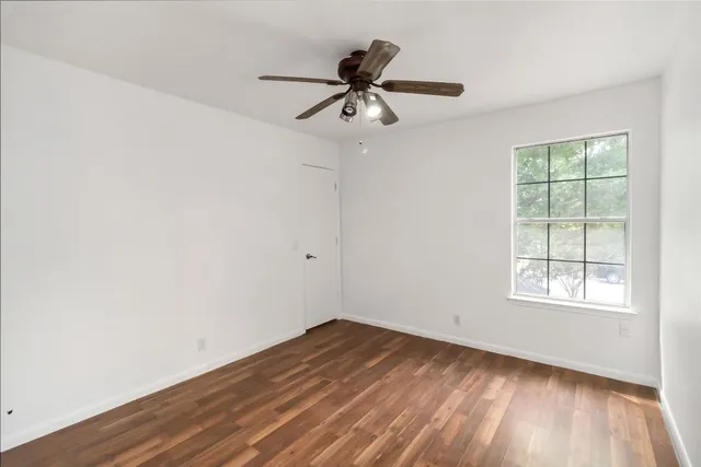 an empty room with wooden floor fan and windows