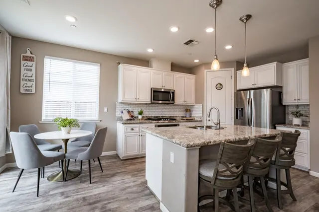 a kitchen with stainless steel appliances granite countertop a stove a refrigerator a kitchen island a dining table and chairs