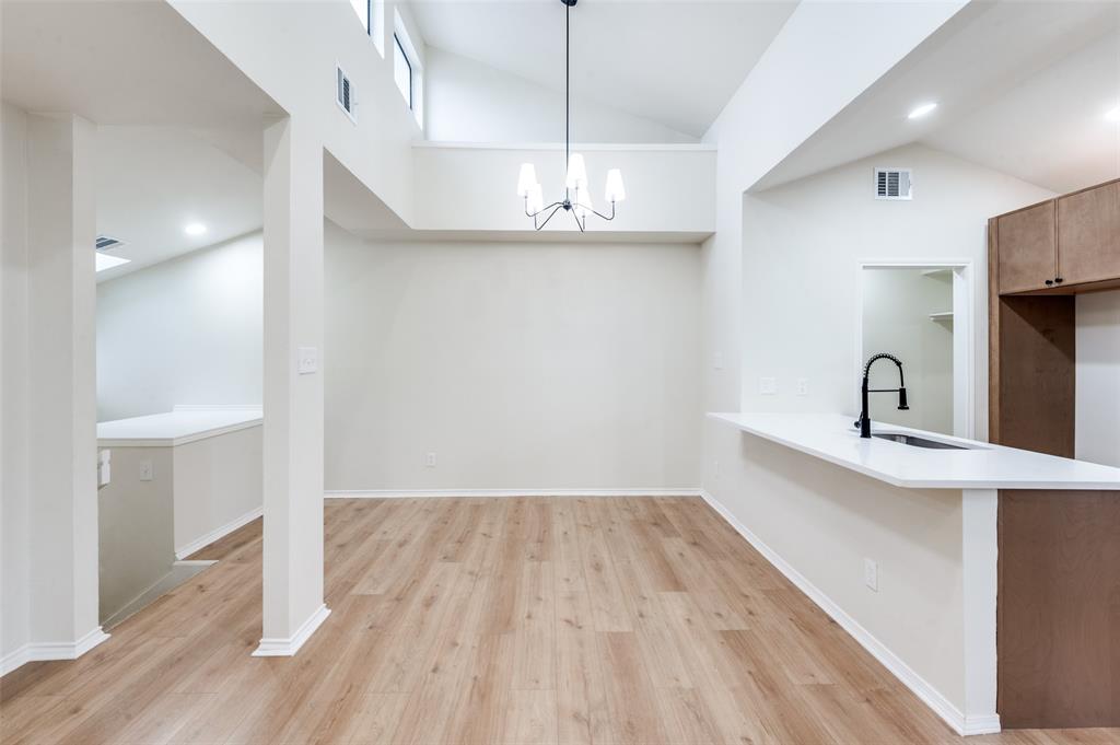17490 Meandering Way, Unit 2202 Dallas, TX 75252 - Photo 10 of 24 Open-concept living area featuring vaulted ceilings with high windows, wood-finish flooring, and a kitchen island with a single-basin sink and a matte black faucet