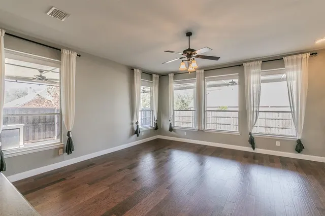 a view of an empty room and kitchen with wooden floor