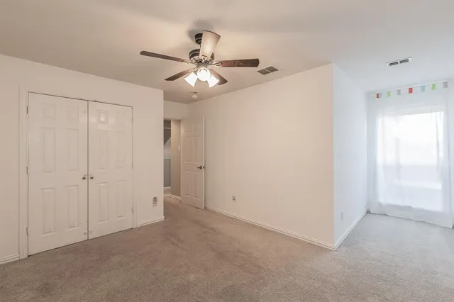 an empty room with chandelier fan and windows