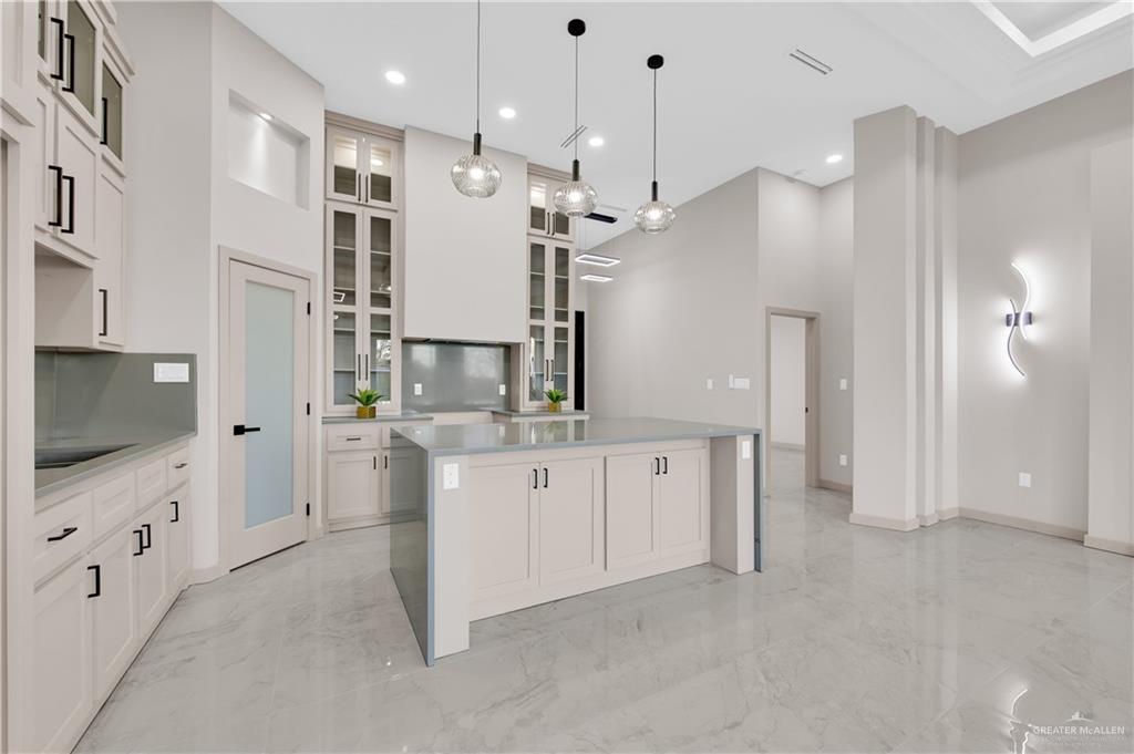 608 Spring Drive Alton, TX 78573 - Photo 11 of 32 Kitchen featuring a kitchen island, a towering ceiling, glass insert cabinets, hanging light fixtures, and light marble finish flooring