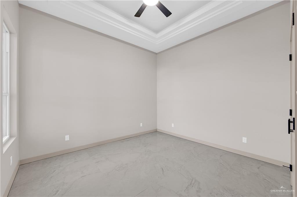 608 Spring Drive Alton, TX 78573 - Photo 17 of 32 Empty room featuring a raised ceiling, crown molding, a ceiling fan, and light marble finish floors