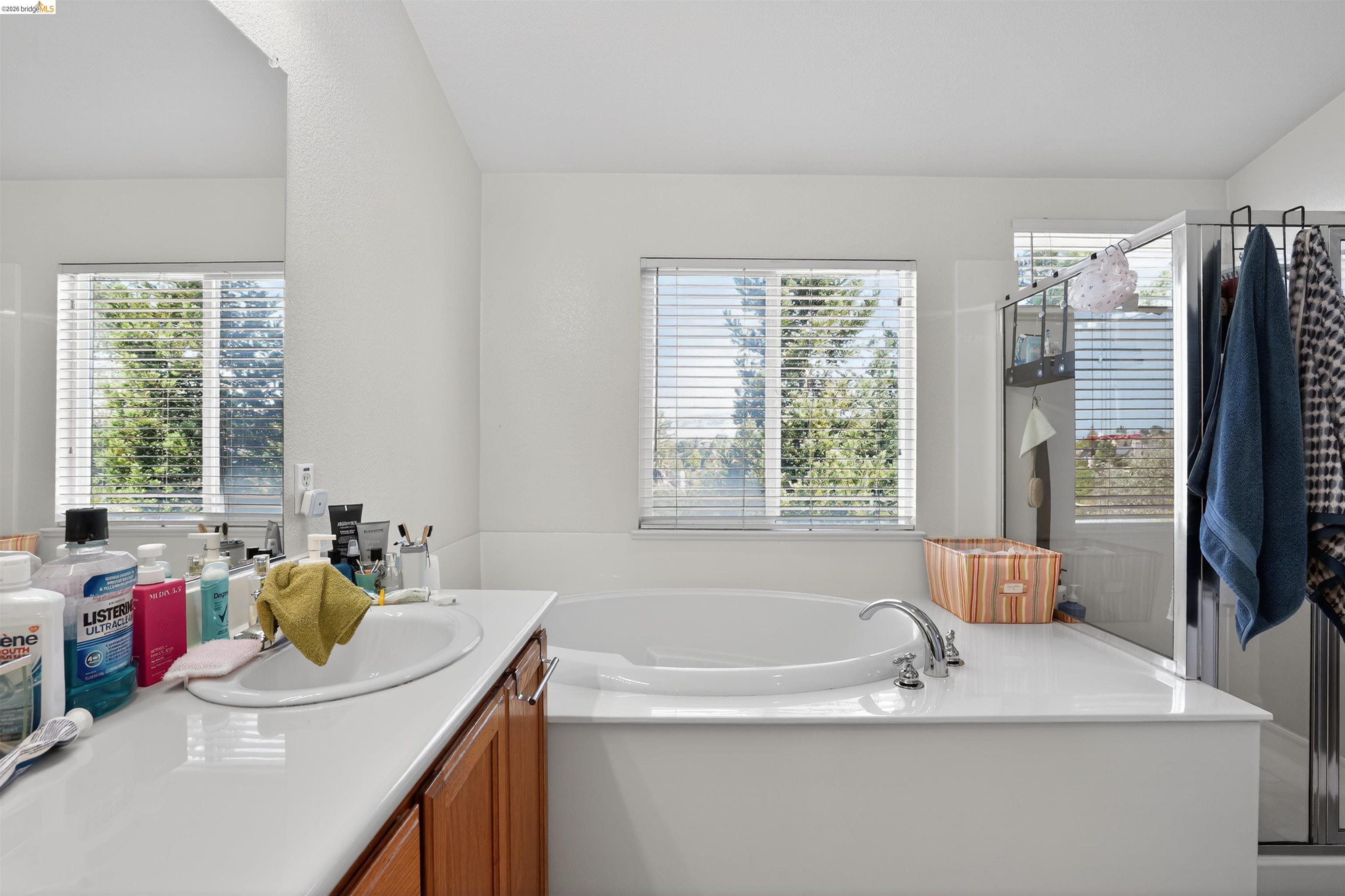 1221 Andrea Way Vallejo, CA 94591 - Photo 19 of 29 Recessed soaking tub with surrounding white countertop, dual windows with horizontal blinds, and an adjacent glass-enclosed shower