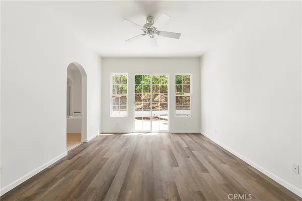 an empty room with wooden floor fan and windows