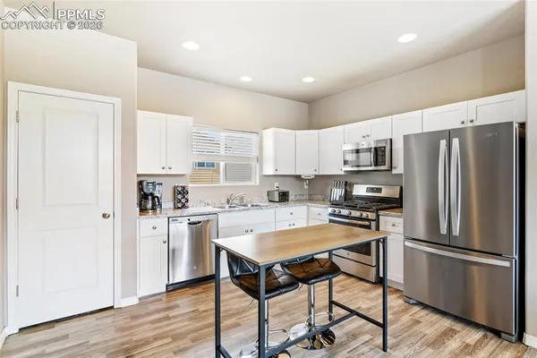 a kitchen with stainless steel appliances a refrigerator a stove a sink and white cabinets with wooden floor