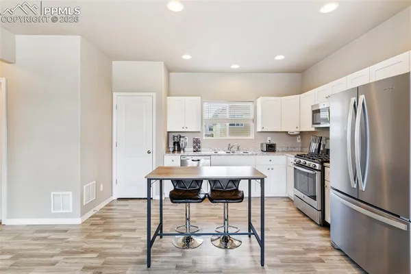 a kitchen with stainless steel appliances a refrigerator a stove a sink and white cabinets with wooden floor