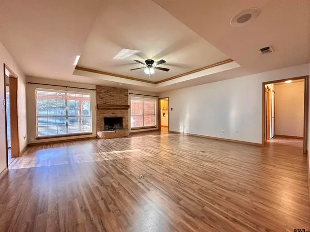 an empty room with wooden floor ceiling fan and windows