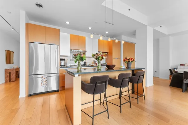 a kitchen with stainless steel appliances granite countertop a refrigerator a stove a sink a dining table and chairs with wooden floor