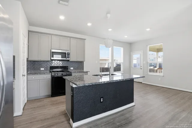 a kitchen with stainless steel appliances granite countertop a stove a sink a refrigerator and white cabinets with wooden floor