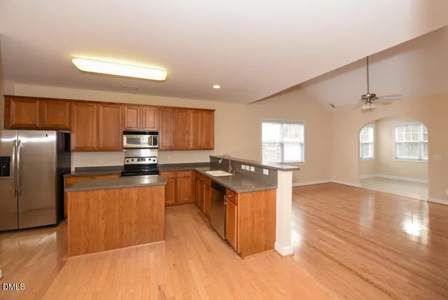 a kitchen with stainless steel appliances granite countertop a refrigerator a sink dishwasher a stove with wooden cabinets and floors