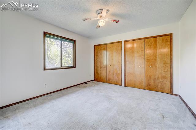 18715 Spring Valley Road Monument, CO 80132 - Photo 20 of 35 Unfurnished bedroom featuring two closets, light carpet, ceiling fan, and a textured ceiling