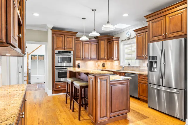 a kitchen with stainless steel appliances granite countertop a refrigerator a oven a stove and a sink with wooden floor