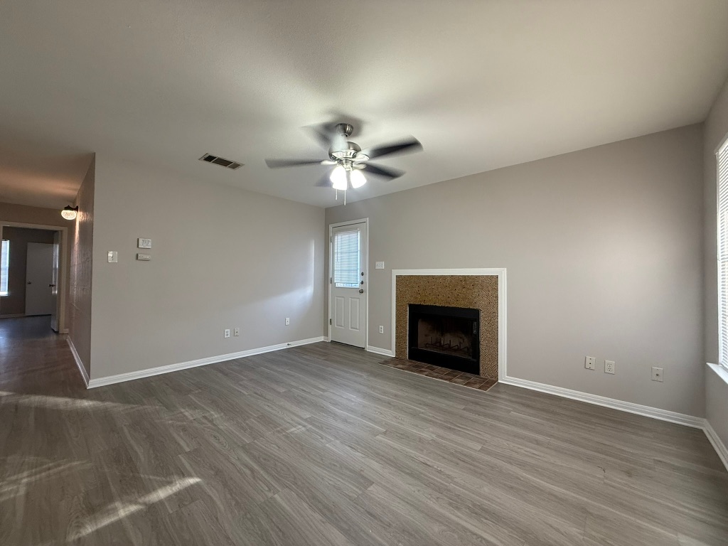 1904 Alex Avenue, Unit A Austin, TX 78728 - Photo 3 of 15 Unfurnished living room featuring a tiled fireplace, a ceiling fan, wood finished floors, and healthy amount of natural light