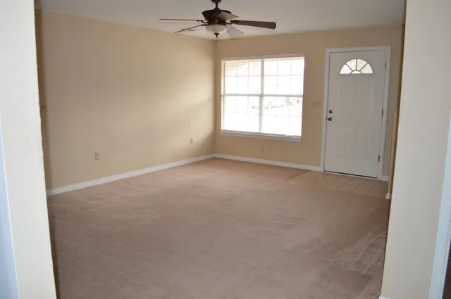 an empty room with a chandelier fan and windows