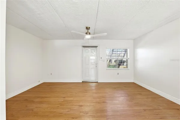 an empty room with wooden floor ceiling fan and windows
