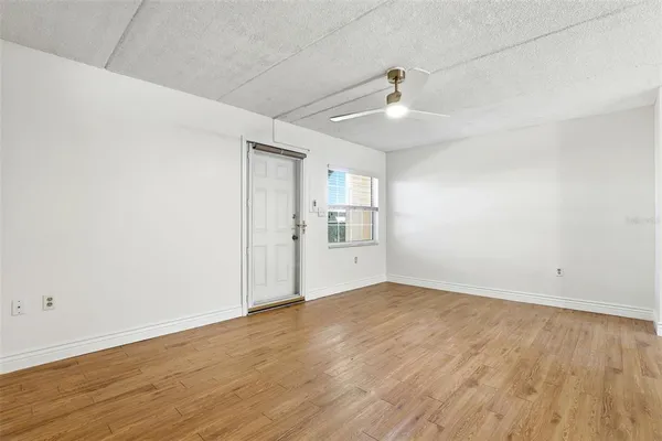 a view of an empty room with wooden floor and a ceiling fan