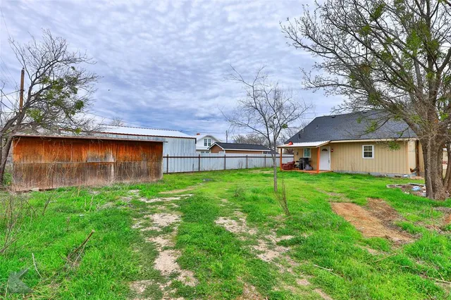a view of backyard with huge green area and wooden fence