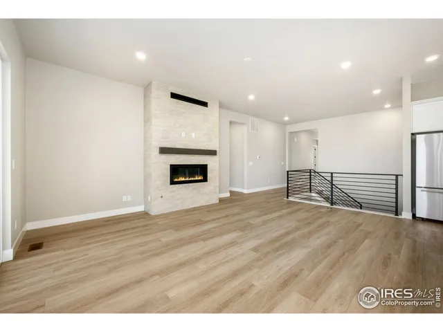 a view of an empty room with wooden floor kitchen view and a fireplace