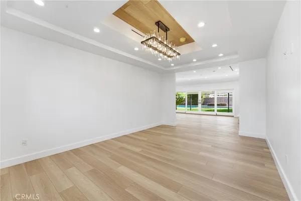 an empty room with wooden floor chandelier and windows