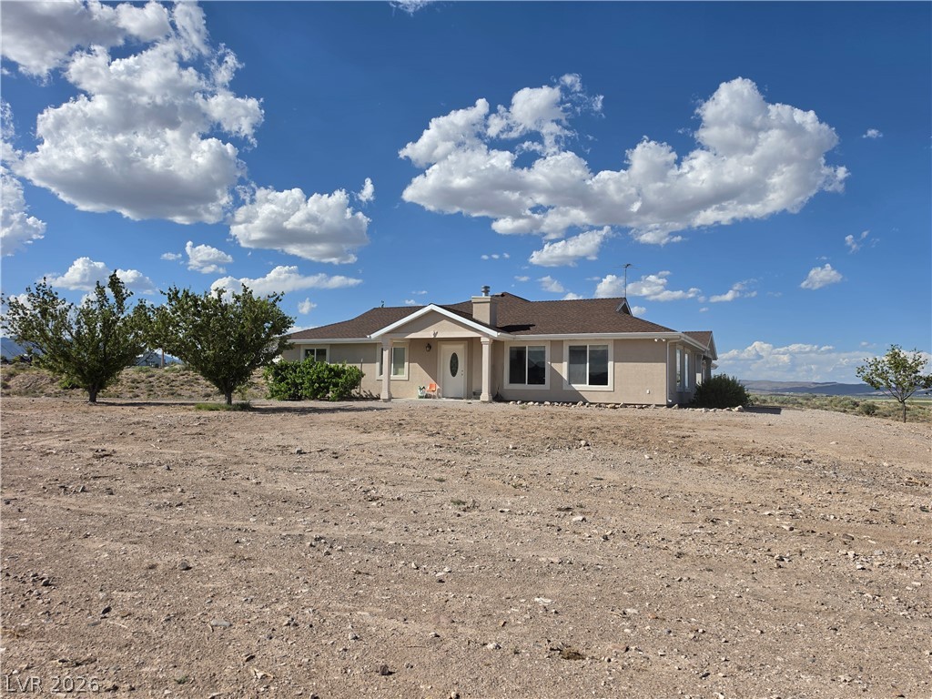 5272 Truman Lane Caliente, NV 89008 - Photo 36 of 43 An inviting single-story residence is framed by expansive desert landscaping and mature trees, all under a vast, cloud-dotted sky.