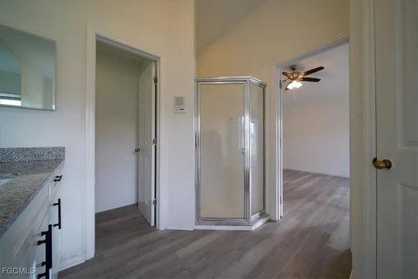 an empty room with wooden floor and way to kitchen