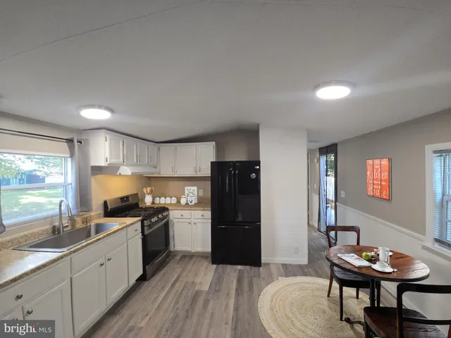 a kitchen with stainless steel appliances granite countertop a refrigerator a sink dishwasher a stove and a dining table with wooden floor