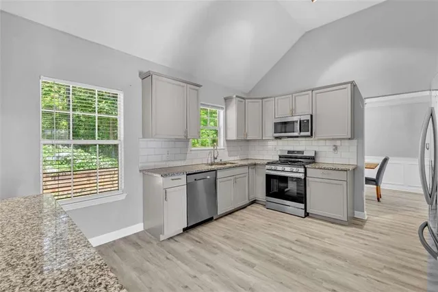 a kitchen with stainless steel appliances kitchen island granite countertop a stove a sink a refrigerator white cabinets a dining table and chairs