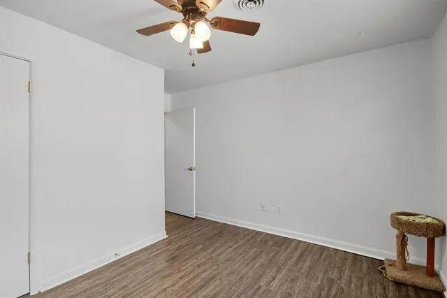 an empty room with wooden floor fan and windows