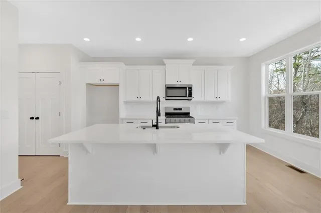 a large kitchen with kitchen island a stove a sink a refrigerator and white cabinets next to a window
