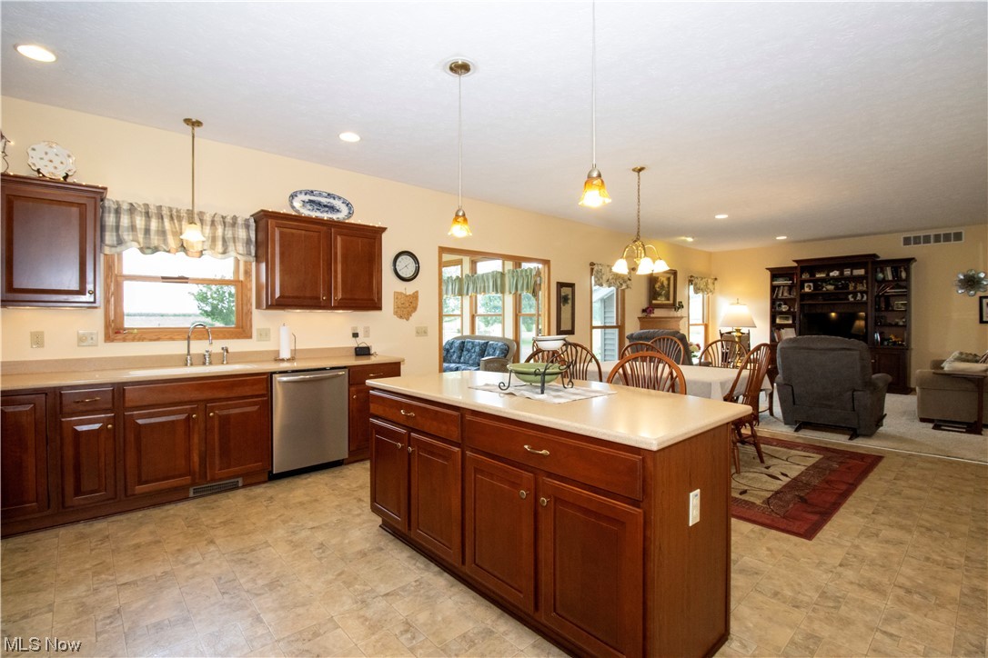 4281 Heyl Road Wooster, OH 44691 - Photo 5 of 32 Kitchen featuring stainless steel dishwasher, an island with sink, dark brown cabinets, light countertops, pendant lighting, and light tile flooring