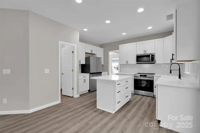 a kitchen with stainless steel appliances a stove top oven a sink a refrigerator white cabinets and wooden floor