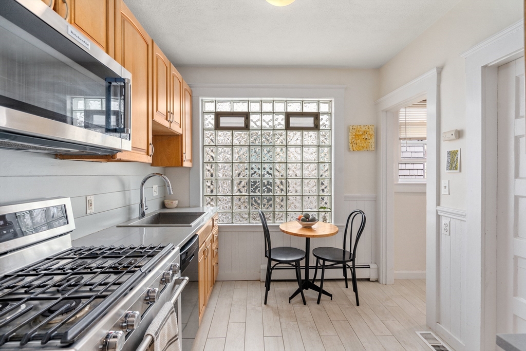 75 Brook Street, Unit 1 Brookline, MA 02445 - Photo 9 of 26 a kitchen with granite countertop a stove a sink dishwasher a dining table and chairs with wooden floor