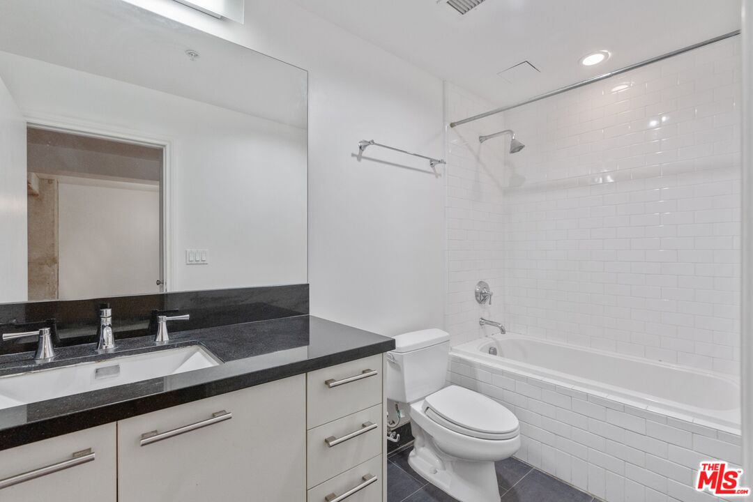 416 South Spring Street, Unit 210 Los Angeles, CA 90013 - Photo 11 of 18 a bathroom with a granite countertop toilet a sink and a mirror