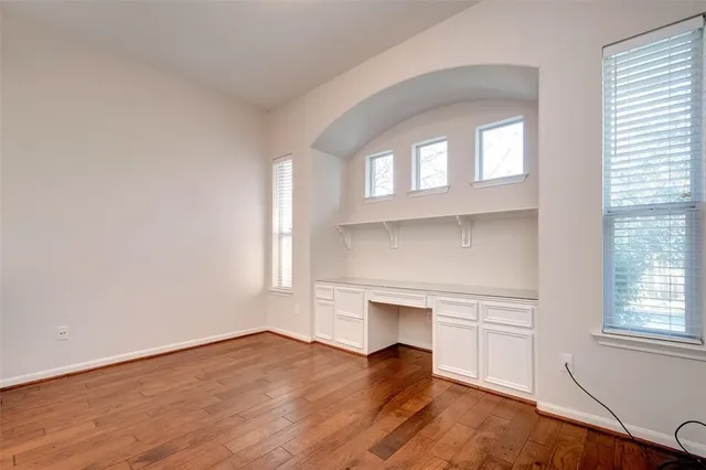 an empty room with wooden floor cabinet and windows
