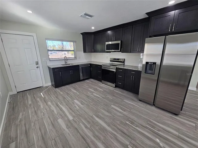 a kitchen with granite countertop wooden floors stainless steel appliances a sink and a window
