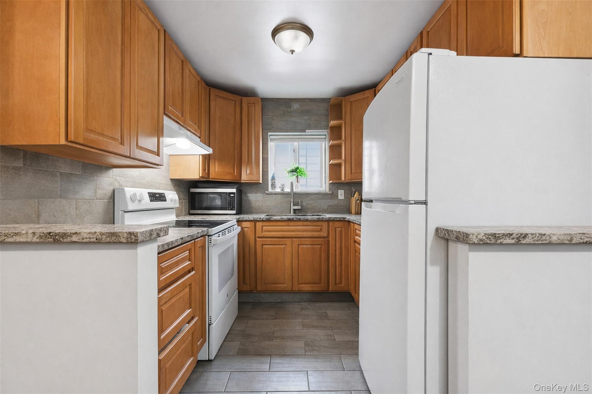 1677 Unionport Road Bronx, NY 10460 - Photo 16 of 33 Kitchen with white appliances, wood finish cabinetry, decorative backsplash, dark wood-style floors, and light stone counters