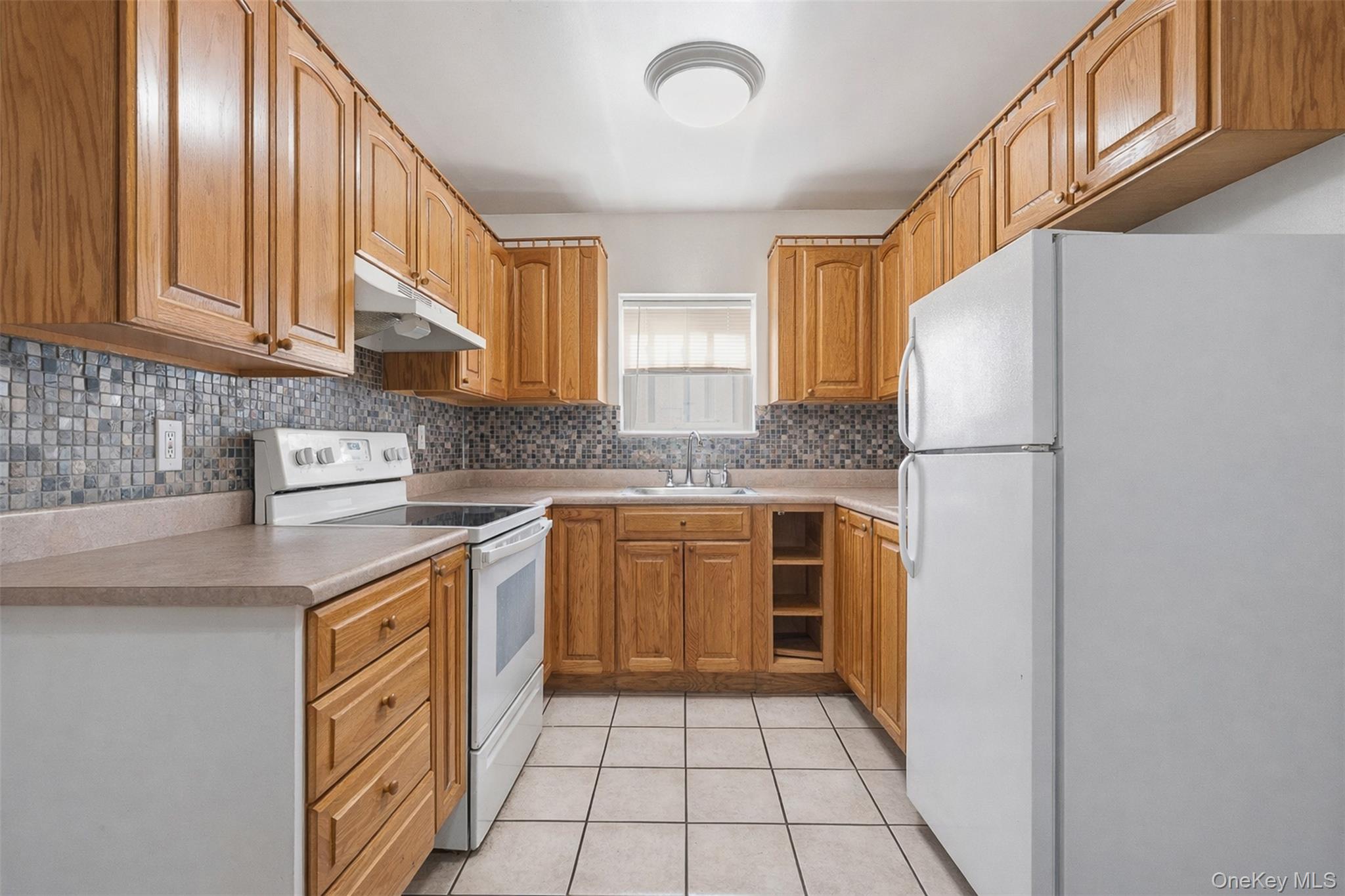 1677 Unionport Road Bronx, NY 10460 - Photo 5 of 33 Kitchen featuring white appliances, light countertops, wood finish cabinets, light tile patterned floors, and tasteful backsplash