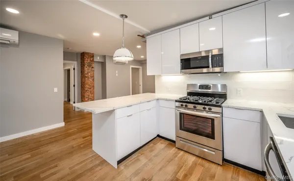 a kitchen with stainless steel appliances white cabinets a sink a stove a microwave and wooden floors