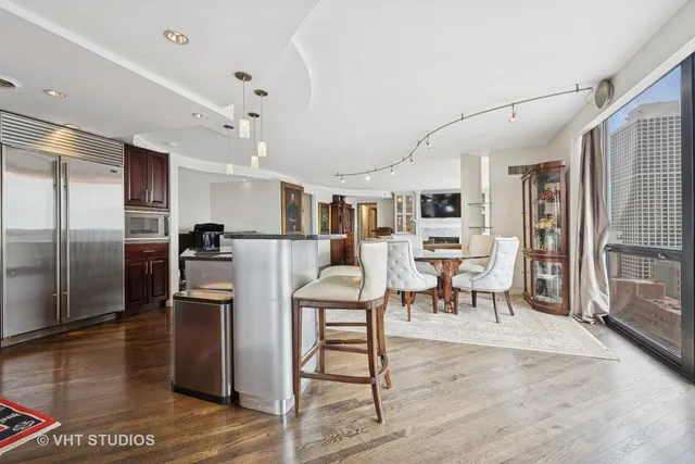 a kitchen with stainless steel appliances kitchen island granite countertop a refrigerator a stove a dining table and chairs with wooden floor